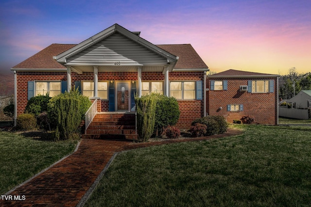 bungalow-style home with a yard, brick siding, and roof with shingles