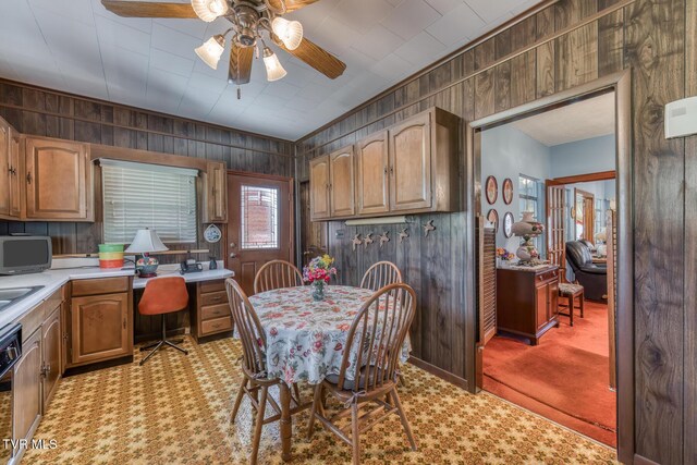 kitchen with light carpet, wooden walls, a ceiling fan, and light countertops