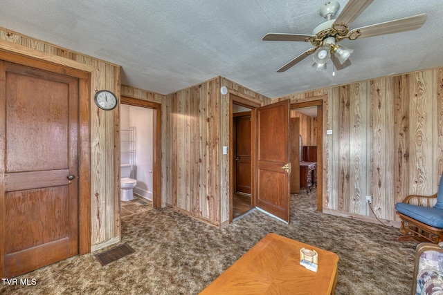 living area with wooden walls, a textured ceiling, and carpet