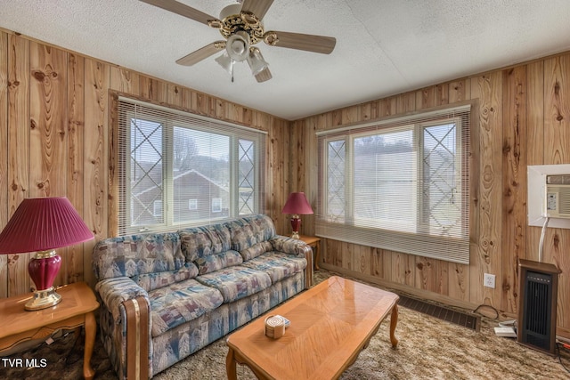 living room with a ceiling fan, wooden walls, a healthy amount of sunlight, and a textured ceiling