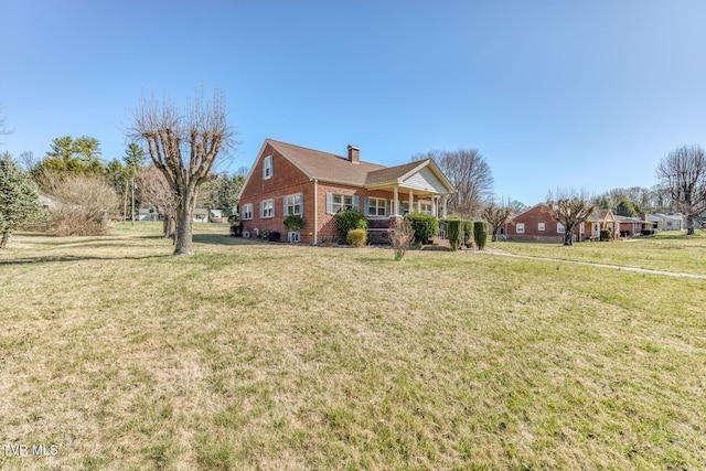 view of front facade featuring brick siding, covered porch, a chimney, and a front yard