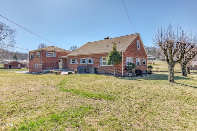 rear view of house featuring cooling unit, brick siding, and a yard