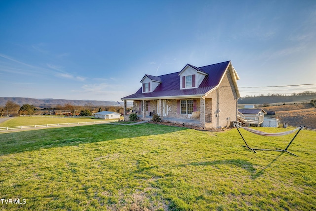 cape cod home featuring a front yard, fence, covered porch, brick siding, and metal roof