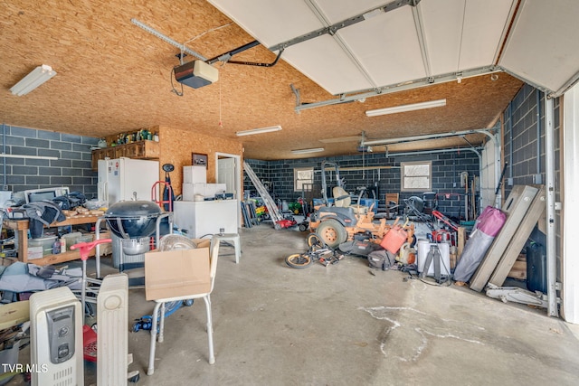 garage with concrete block wall, a garage door opener, and freestanding refrigerator