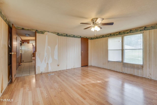 empty room featuring visible vents, a textured ceiling, a ceiling fan, and light wood finished floors