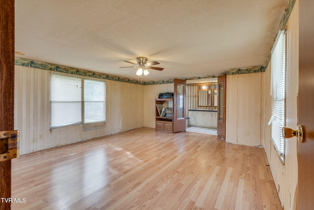 unfurnished living room featuring a textured ceiling, light wood-type flooring, and a ceiling fan