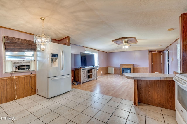 kitchen with white appliances, lofted ceiling, tile counters, wainscoting, and a glass covered fireplace