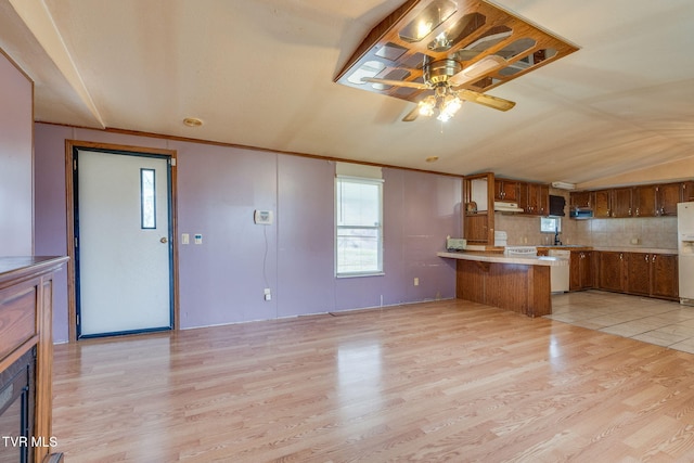 kitchen with light wood-style flooring, backsplash, a peninsula, brown cabinetry, and light countertops