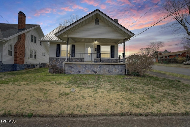 view of front of property with a porch, stone siding, central air condition unit, a lawn, and metal roof