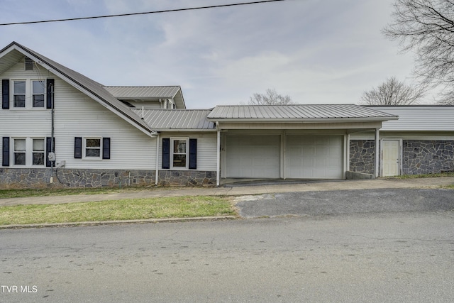 view of front of house featuring metal roof, stone siding, an attached garage, and aphalt driveway