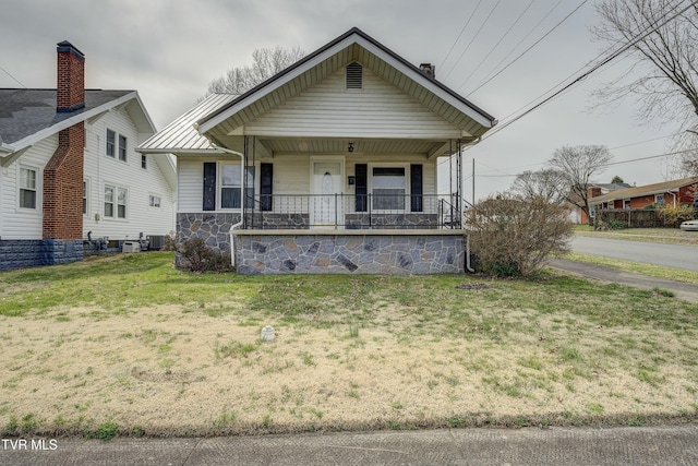 view of front of house featuring a front yard, covered porch, stone siding, and central AC