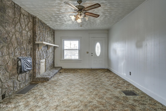 carpeted entrance foyer featuring visible vents, baseboards, ceiling fan, a fireplace, and a textured ceiling