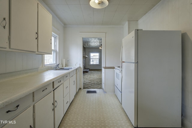 kitchen featuring white appliances, a healthy amount of sunlight, light floors, a sink, and light countertops