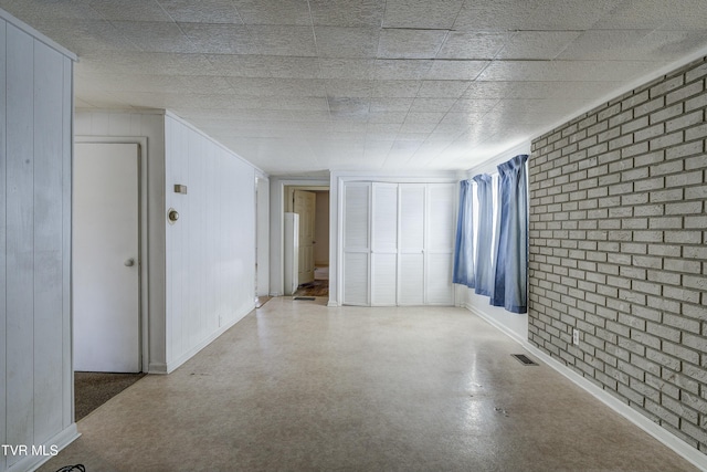 spare room featuring visible vents, baseboards, and brick wall