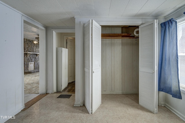 unfurnished bedroom featuring a closet, wooden walls, and light colored carpet