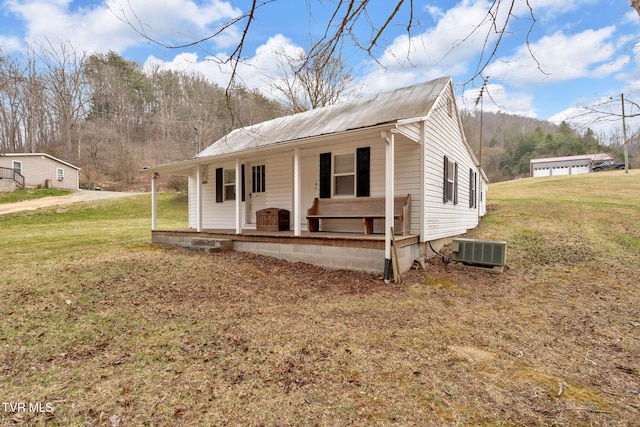 view of front of house featuring a front lawn, central air condition unit, covered porch, and metal roof