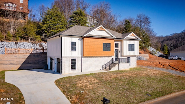 view of front of home featuring board and batten siding, a front lawn, brick siding, and driveway