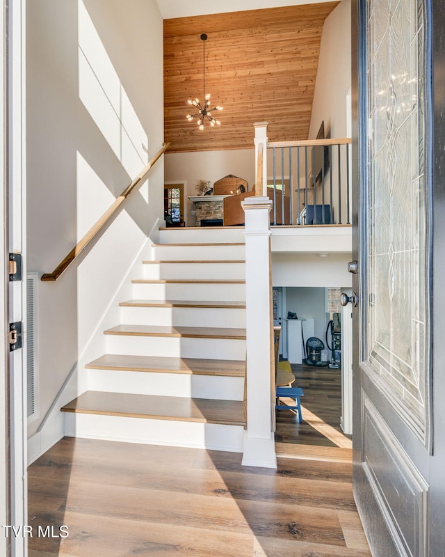 staircase featuring wood ceiling, high vaulted ceiling, an inviting chandelier, and wood finished floors