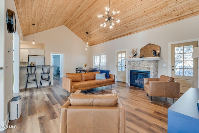 living room with a notable chandelier, high vaulted ceiling, wood finished floors, a stone fireplace, and wood ceiling