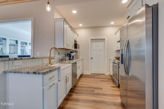 kitchen featuring stone countertops, a sink, decorative backsplash, stainless steel appliances, and light wood-type flooring