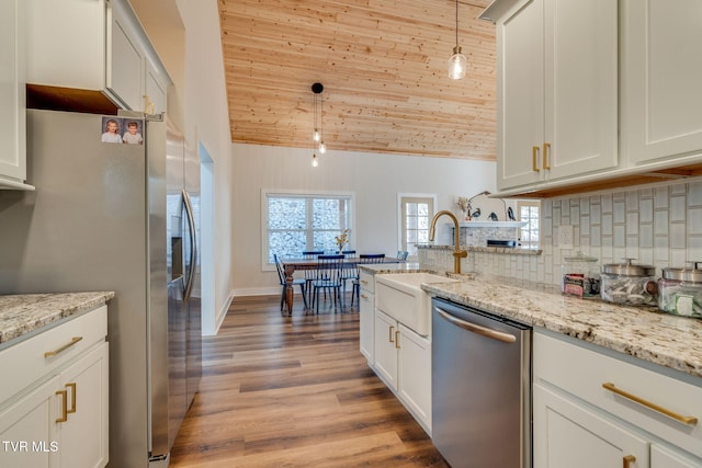 kitchen featuring a sink, hanging light fixtures, light wood-style floors, appliances with stainless steel finishes, and backsplash