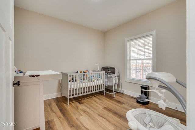 bedroom with a nursery area, light wood-type flooring, and baseboards