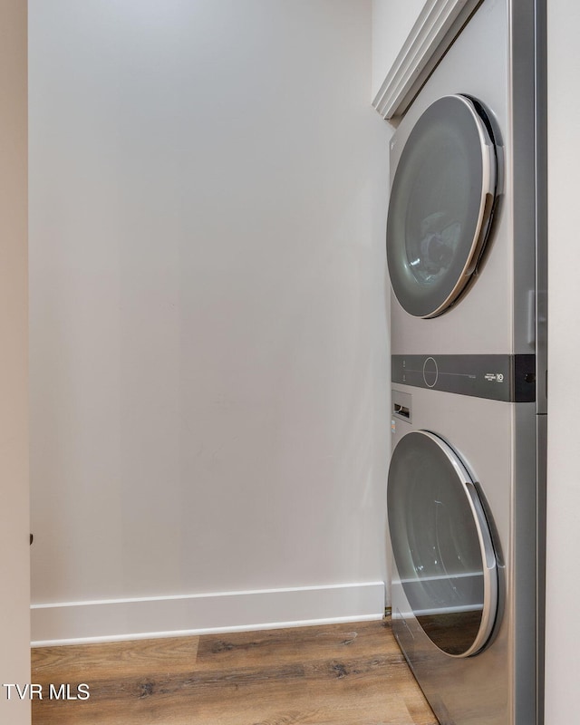 washroom featuring laundry area, wood finished floors, stacked washer / drying machine, and baseboards