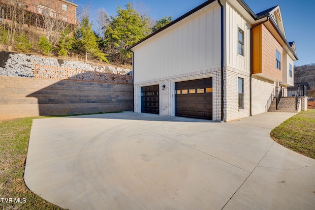 view of side of home featuring board and batten siding, concrete driveway, and brick siding