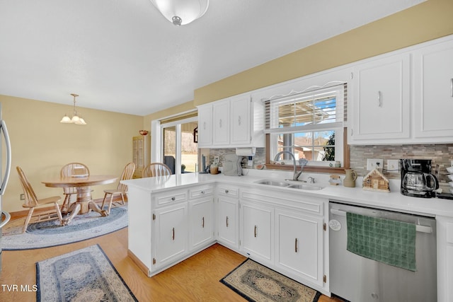 kitchen with a notable chandelier, a sink, stainless steel dishwasher, white cabinetry, and a peninsula