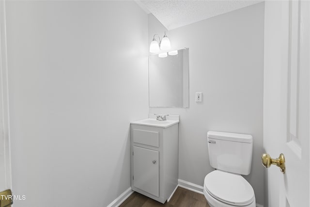 bathroom with toilet, a textured ceiling, wood finished floors, baseboards, and vanity