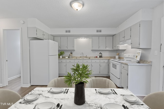 kitchen featuring under cabinet range hood, visible vents, white appliances, and a sink