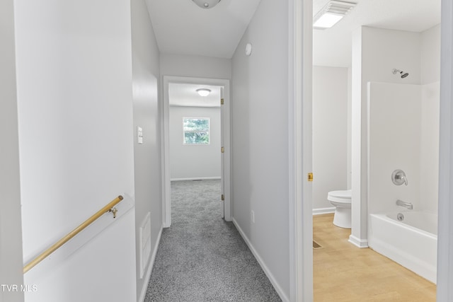 hallway featuring light carpet, light wood-style flooring, and baseboards