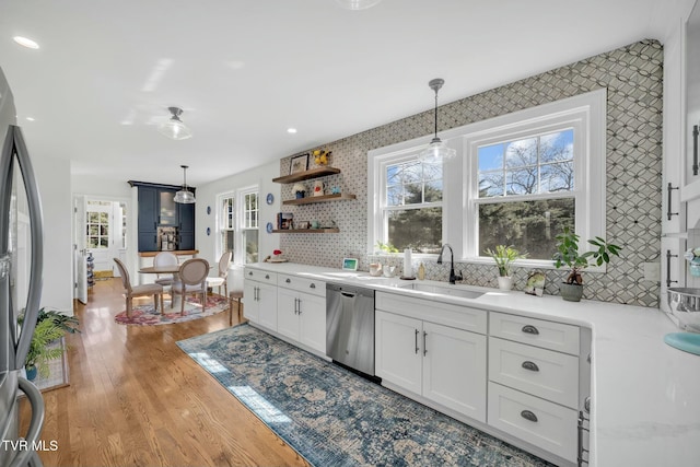 kitchen with pendant lighting, light wood-style flooring, a sink, appliances with stainless steel finishes, and white cabinets