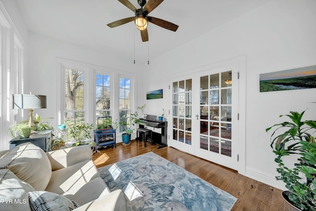 interior space featuring wood finished floors, baseboards, a wood stove, ceiling fan, and french doors