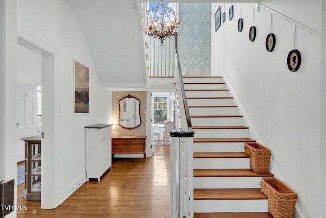 staircase featuring wood finished floors, baseboards, and a chandelier