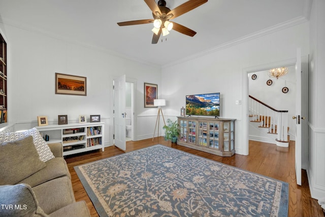 living area featuring stairs, crown molding, ceiling fan with notable chandelier, and wood finished floors