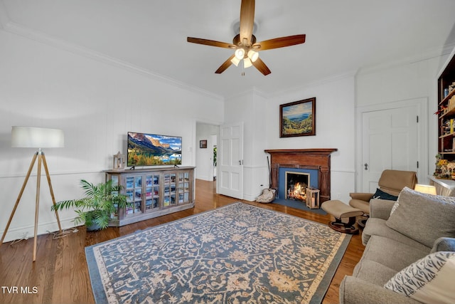 living room featuring crown molding, a fireplace with flush hearth, wood finished floors, and ceiling fan