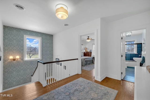 hall with visible vents, an upstairs landing, wood finished floors, and wallpapered walls