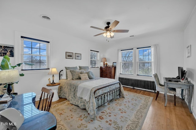 bedroom featuring visible vents, multiple windows, radiator heating unit, and wood finished floors