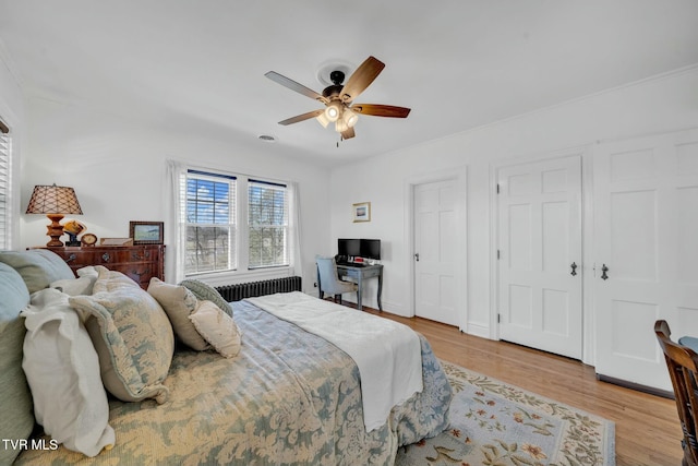 bedroom with radiator heating unit, a ceiling fan, and light wood finished floors