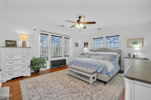 bedroom featuring radiator, wood finished floors, visible vents, and ceiling fan