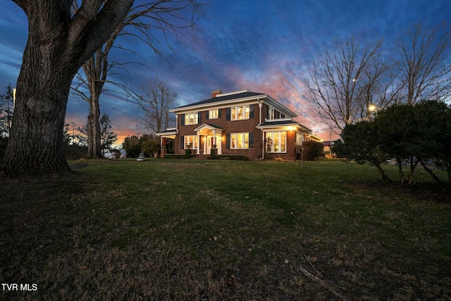 colonial home with brick siding, a chimney, and a front lawn