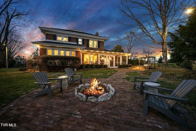 back of property at dusk with a patio area, a fire pit, brick siding, and a sunroom