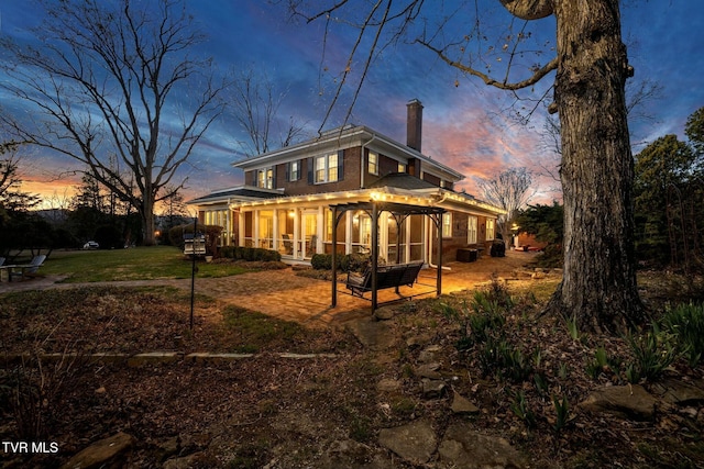 back of house at dusk with a lawn, a chimney, and a sunroom