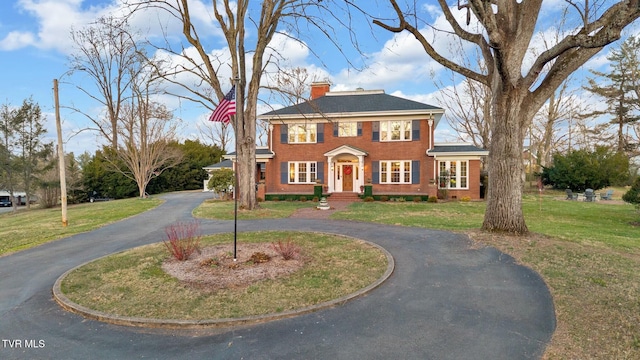 colonial home featuring a front lawn, curved driveway, brick siding, and a chimney