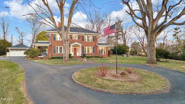 view of front of property with curved driveway, a chimney, a front lawn, a garage, and brick siding