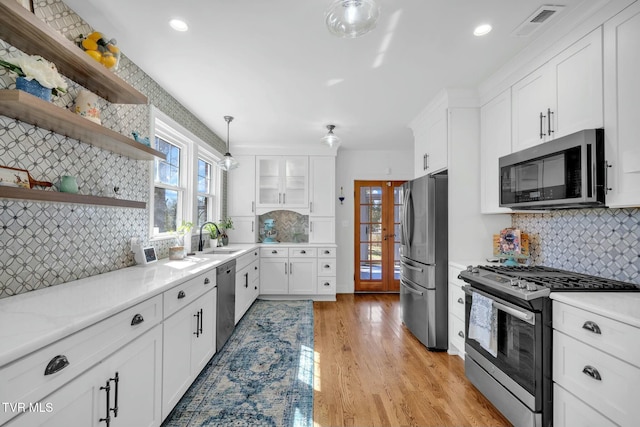 kitchen with light wood-type flooring, open shelves, backsplash, appliances with stainless steel finishes, and white cabinets