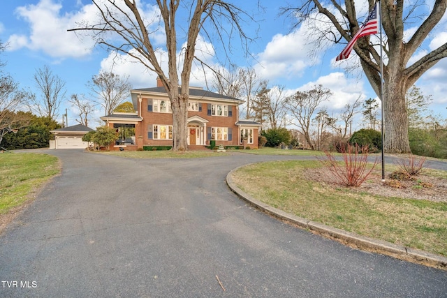 colonial inspired home featuring a front lawn, a garage, and curved driveway