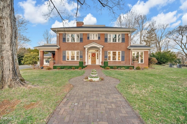 view of front of home featuring brick siding, a chimney, and a front yard