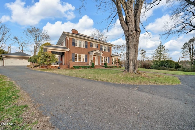 colonial inspired home featuring brick siding, a front lawn, a chimney, and a garage